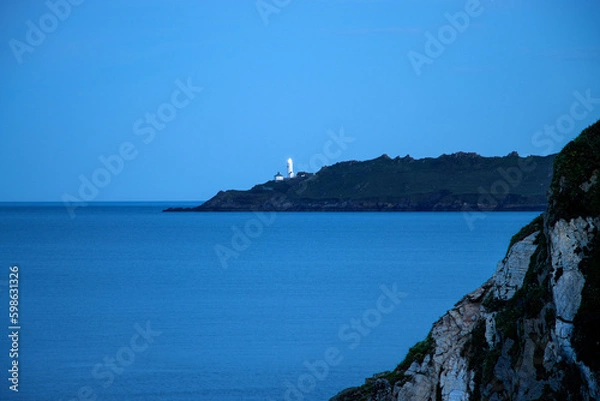 Fototapeta Towards Start Point Lighthouse at sunset.  A calm still sea on a cool summer evening.  The lighthouse guiding mariners.
