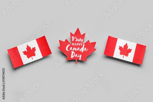 Fototapeta Paper maple leaf with text 1TH JULY HAPPY CANADA DAY and flags on grey background