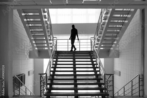 Fototapeta Architecture inside the building. Staircase and a walking person. Steps, steel railings. Up down. Silhouette of a man. Black and white photography