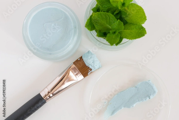 Fototapeta Glass jar with natural facial mask and leaf mint on glas plate and a brush for application on white background, close up. Selective fokus
