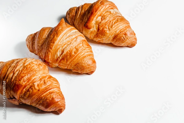 Fototapeta Three large croissants on a white background with space for text. Fresh pastries in butter. Creative concept for bakery and cafe
