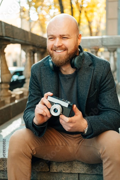 Obraz Vertical shot of a bald smiling man ready to take some pictures with his camera.
