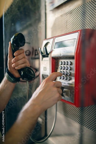 Fototapeta Person dialing a phone number on a public telephone at a payphone booth. Old school telecommunications technology. 
