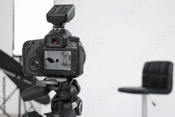 Fototapeta Tripod with camera, bar stool and professional lighting equipment in modern photo studio, focus on screen. Space for text
