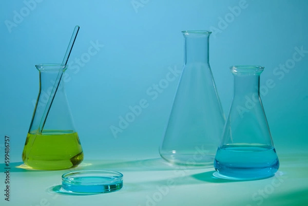 Fototapeta Three erlenmeyer flask filled with blue and yellow fluid. Empty area to display product. Concept of chemical, scientific experiment