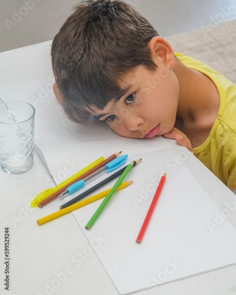 Obraz The boy is tired of studying. The child got tired and lay down on the textbook. The boy is engaged in creativity and thinks what to draw, The boy is looking for an idea for drawing. Child at the table