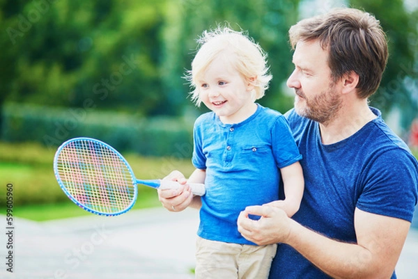 Fototapeta Little boy playing badminton with dad on the playground