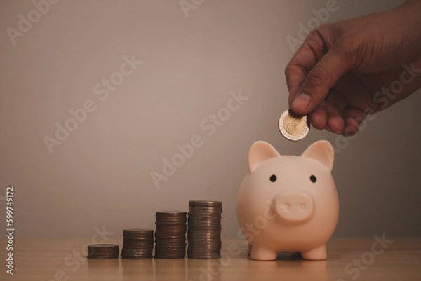 Fototapeta piggy bank with hand of a man under saving coin in piggy bank, symbol of saving for future investment or retirement by small deposit money continuously