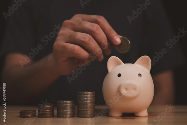 Fototapeta a man is under saving money coin in to piggy bank, symbol of financial management and future aim