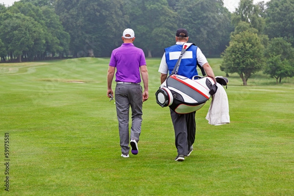 Fototapeta Golfer and caddy walking up a fairway