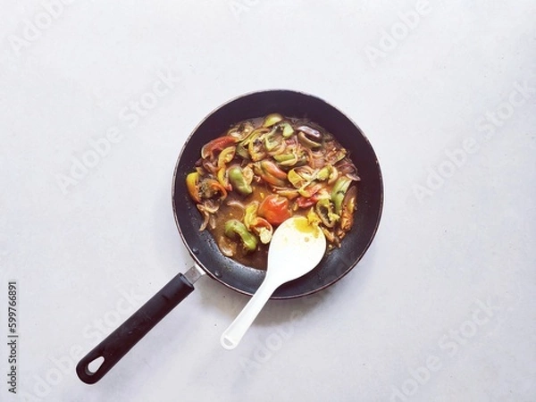 Obraz Bell pepper curry in a cooking pan with spoon. Capsicum sauce seasoning. Vegan recipe. White background.