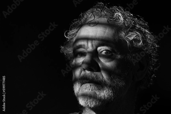 Fototapeta Black and white portrait of an attractive older Caucasian man with grey hair and beard. Turned to the right side with a serious or pensive expression. Dramatic striped shadows.