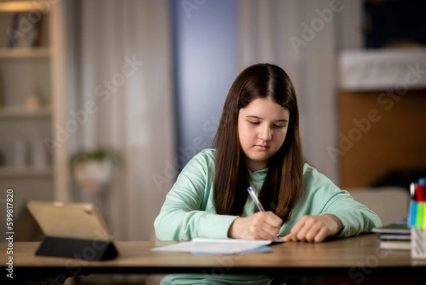 Fototapeta Little girl doing homework with digital tablet. Elementary school student studying online