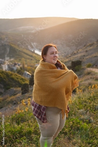 Obraz A plump woman enjoys the sunset. A tourist stands on top of a mountain and looks at the sunset.