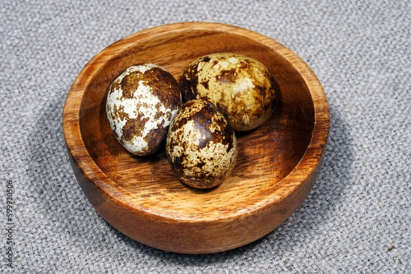 Fototapeta Quail eggs in a round wooden bowl on canvas, close-up, macro. Eggshell stains. Spotted pattern on the eggs. Dietary healthy foods. Egg