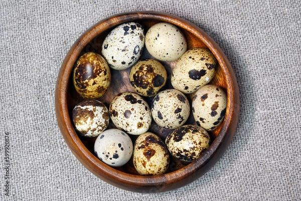 Fototapeta Quail eggs in a round wooden bowl on canvas, close-up, macro. Eggshell stains. Spotted pattern on the eggs. Dietary healthy foods. Egg