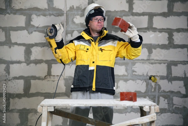 Fototapeta Locksmith in special clothes and goggles works in production. Worker. A man in a helmet and with a grinder in his hand. Industry. Builder. Metal processing with angle grinder