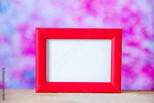 Fototapeta Close up view of red empty picture frame standing on white table on pastel colors background with free space