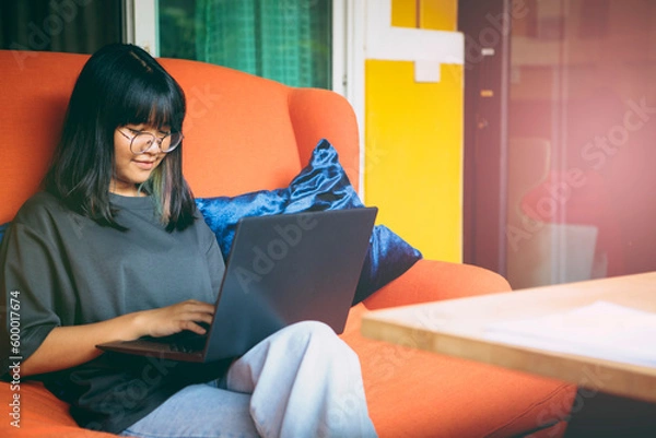 Fototapeta asian teenager using laptop computer by typing for internet communicate at home living room