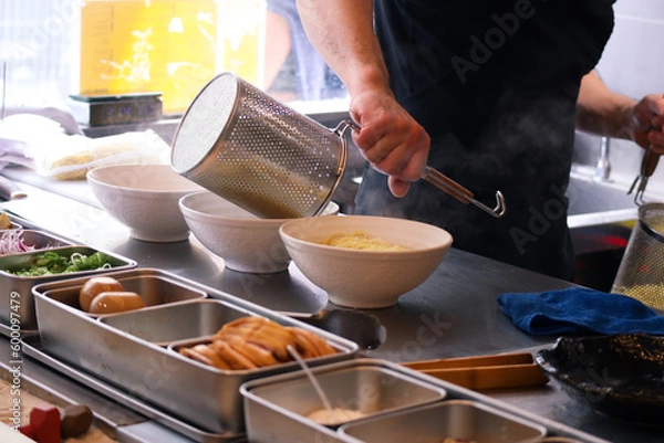 Fototapeta Bowl of Japanese ramen with hands putting the noodles inside it with ramen boiler on a countertop. With all ingredients to preparing Japanese ramen to serve in a restaurant 