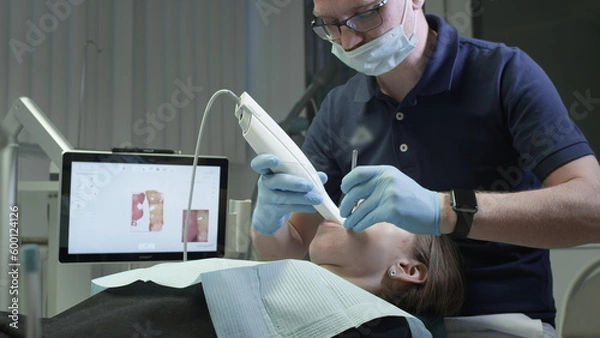 Obraz Doctor scans the patient's teeth in the clinic. The dentist holds in his hand a manual 3D scanner for the jaw and mouth. Dental health. Creates a 3D model of teeth and gums on a medical monitor
