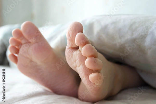 Fototapeta Feet under a light blanket on the bed. Concept of sleeping or waking in the morning