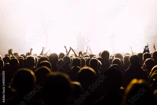 Fototapeta View to stage from the crowd at the music concert. silhouettes of band at background, focus on people.