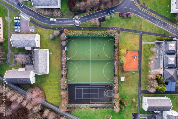 Fototapeta Sport ground in a college or university student camp. Aerial top down view on basketball, tennis and mini soccer or football court and walking path and houses and road.