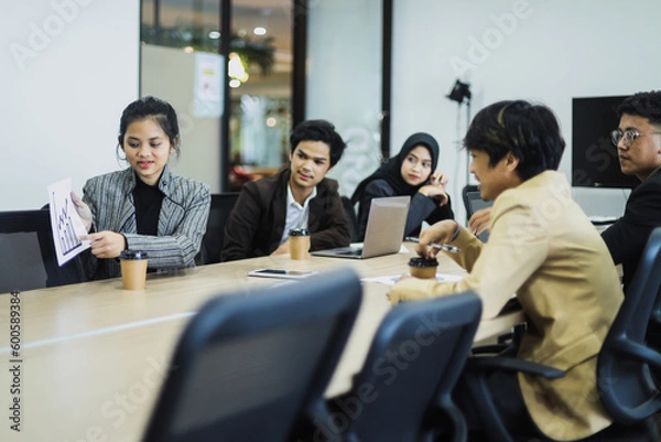 Fototapeta Young woman lead group of young Asian business creative team showing sales graph in brainstorm meeting presentation. 