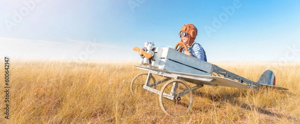 Obraz Little boy is playing the plane.
Happy and funy child imagines himself an aircraft pilot and plays in a aviator costume in an open-air field against a blue sky on a summer sunny day. 