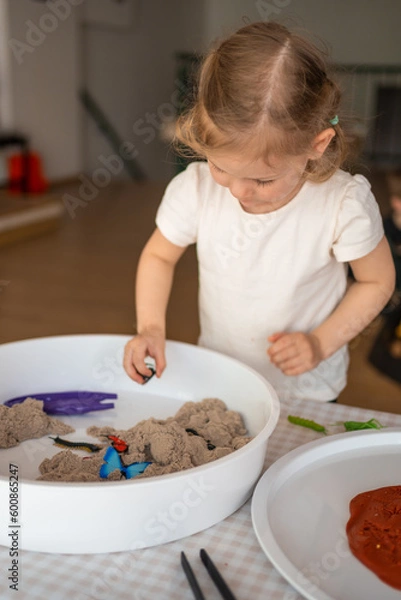 Fototapeta Little girl playing with kinetic sand and toys insect. Sensory development and experiences, themed activities with children, fine motor skills development