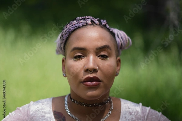 Fototapeta A fresh-faced, dewy person stands in the sunlight, against a defocused backdrop of grass and meadow. Their multiracial, Afro-Latinx complexion is glowing. They are nonbinary, adding more narrative.