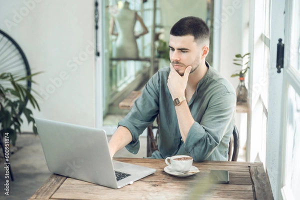 Fototapeta handsome young businessman Working on laptop and working online while sitting at coffee shop table, businessman working outdoors side view