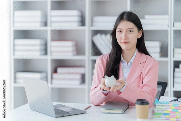 Obraz Sharing good business news. Attractive young businesswoman talking on the mobile phone and smiling while sitting at her working place in office and looking at laptop PC.