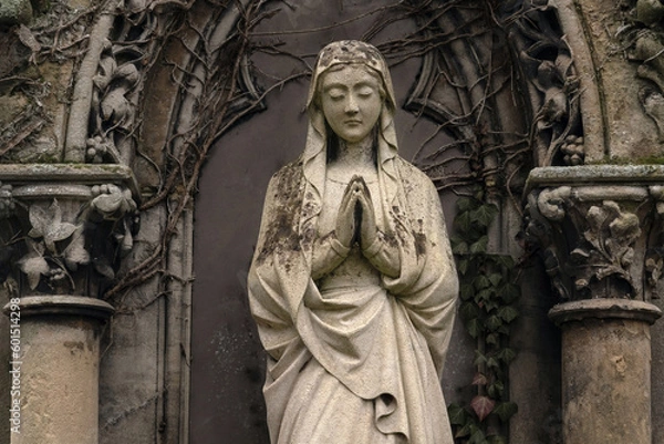 Fototapeta A old sculpture of  Virgin Mary. The stone statue is partially destroyed by time. Background in Gothic style