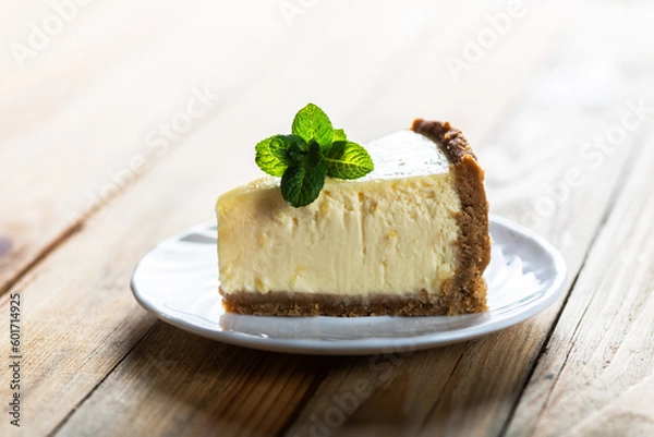 Fototapeta Piece of classic New York cheesecake with a sprig of mint on a plate on a wooden table. The concept of bakery and sweet cakes desserts
