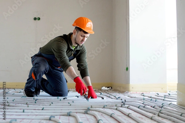 Obraz Worker is installing underfloor heating system. Warm floor heating system