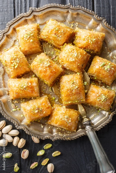 Fototapeta Baklava is a layered pastry dessert made of filo pastry, filled with chopped nuts and sweetened with syrup or honey closeup on the plate on the wooden table. Vertical top view from above