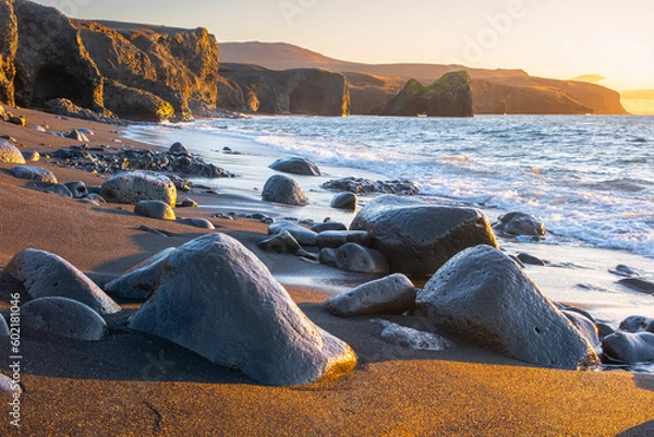 Fototapeta Scenic beach with black sand by low tide at sunset. Sharp volcanic cliffs on Atlantic ocean coastline. Famous touristic place in Iceland