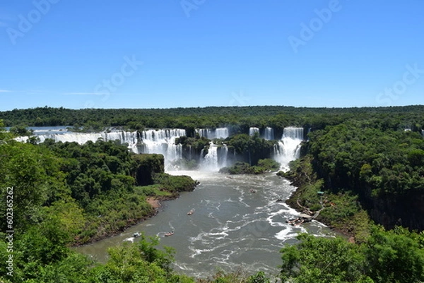 Fototapeta View of the Iguazu Falls hidden among the trees. Boats with tourists sail under the waterfall.