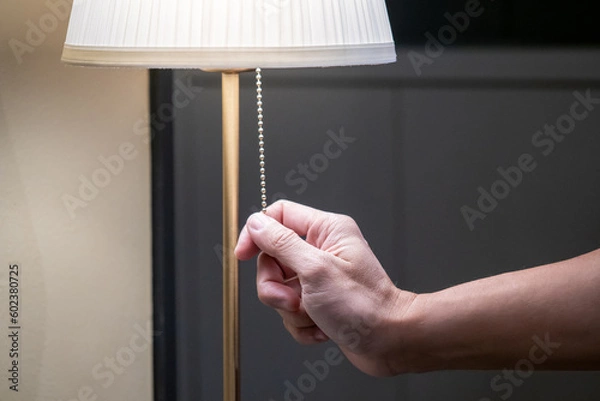 Obraz Saving electricity energy concept. Male hand pulling light switch chain on white lamp in the bedroom. Turn off lighting equipment for bedtime.