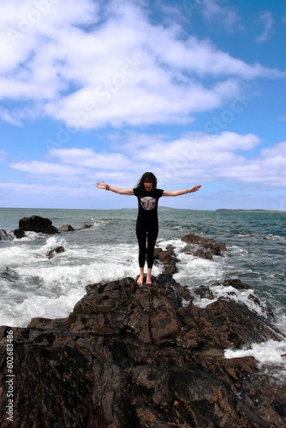 Fototapeta a beautiful woman doing yoga on the edge of the rocks with waves splashing to show a healthy way to live a happy and relaxed lifestyle in a world full of stress