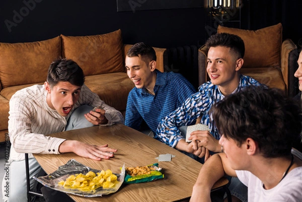 Fototapeta Five friends spending time together, having fun, playing table games and eating fast food and snacks. Small group of friend in a living room. man losing and raging at his friends.