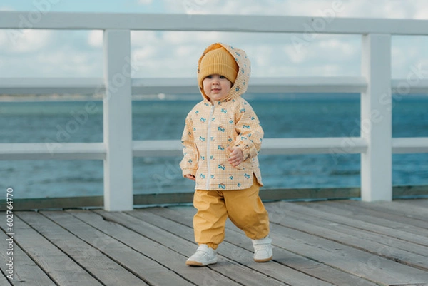 Obraz A toddler in a yellow jacket and pants walks on the pier