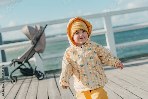 Obraz A toddler in a yellow jacket and pants walks on the pier