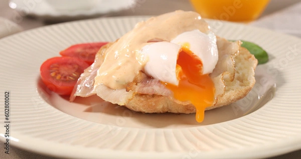 Fototapeta cut poached egg with bacon on a plate. boiled egg on bread with sauce. delicious breakfast with vegetables. serving food on a sunny day.