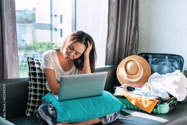 Fototapeta Stressed Asian woman worried about online booking errors or making the wrong travel plans on her summer vacation. Sadness girl fell down due to the trip has been cancelled. Travel and holiday concept.