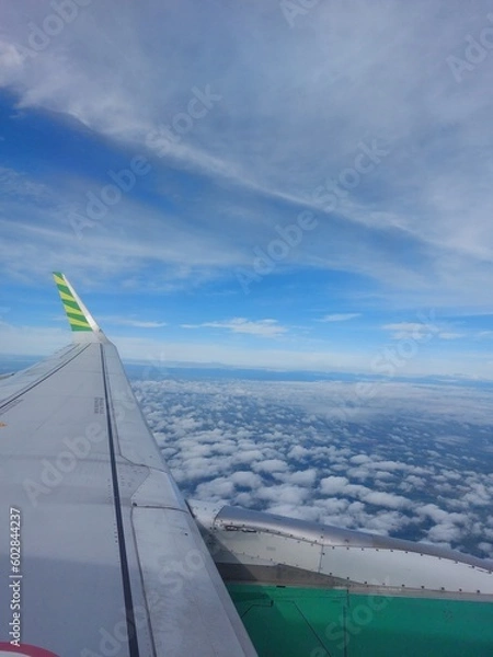Fototapeta Airplane wing view from windows while flying in the air among the clouds and blue sky