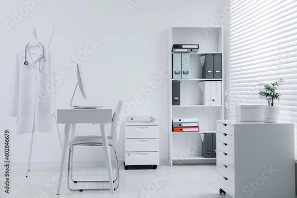 Fototapeta White doctor's gown and stethoscope hanging on rack in clinic