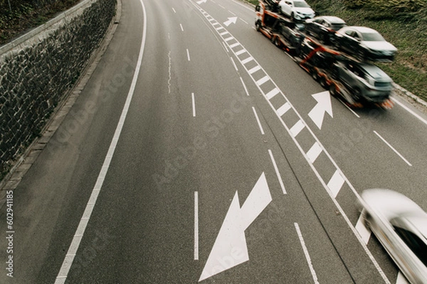 Fototapeta aerial image of a road with an arrow symbol and a truck carrying new cars from the factory , the vehicle is blurred due to movement